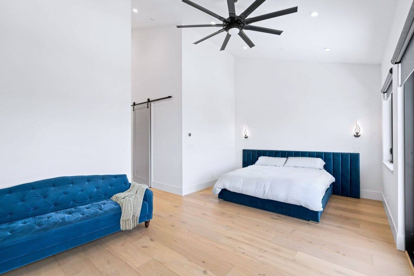 Vaulted primary bedroom with blue upholstered bed and wood flooring
