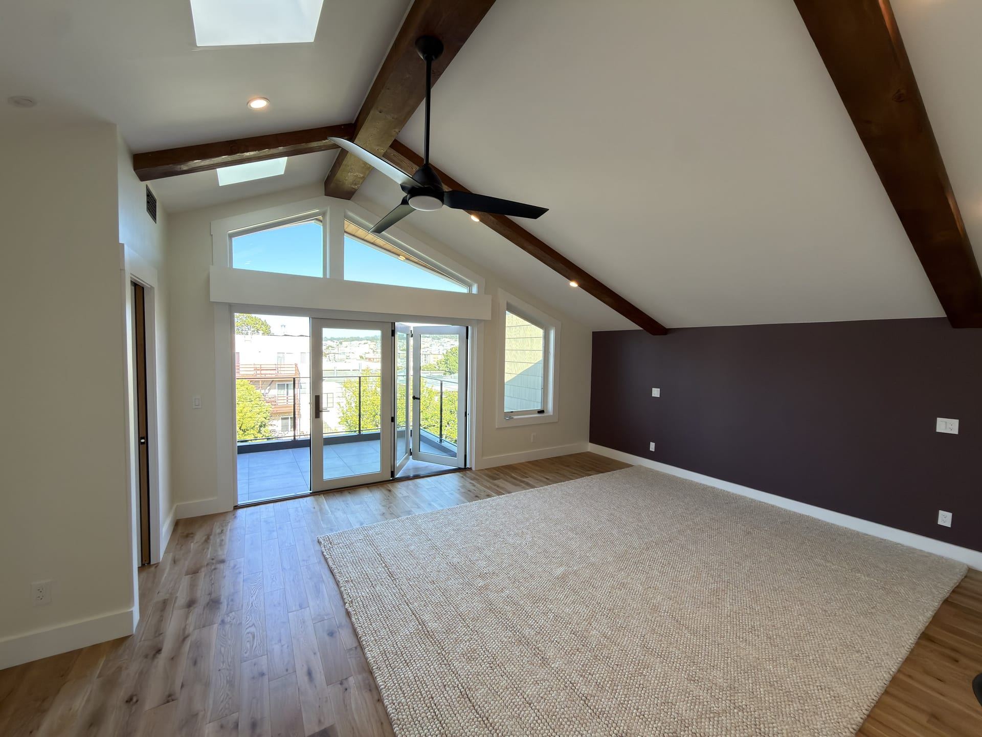 Vaulted primary bedroom with exposed wood beams and deck access
