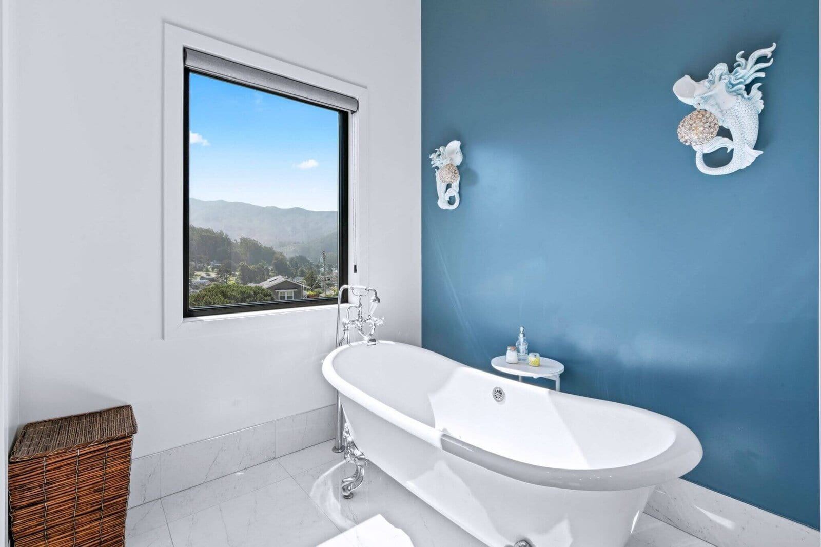 Freestanding tub bathroom with blue feature wall and hillside view