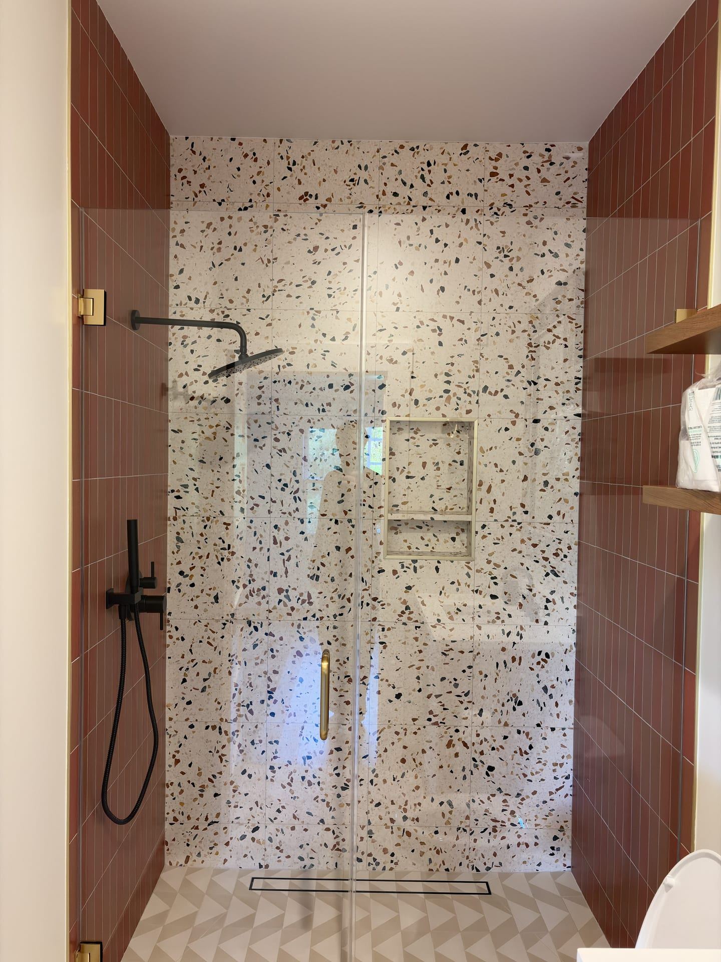 Terrazzo look walk in shower with terracotta tile and black fixtures
