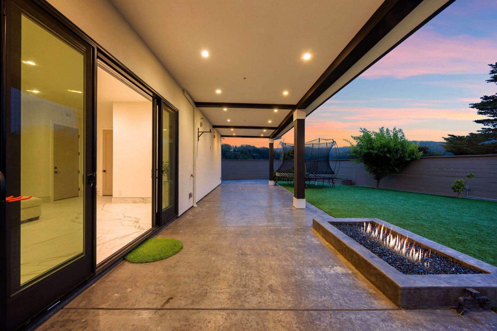 Covered outdoor living patio with linear fire pit at sunset